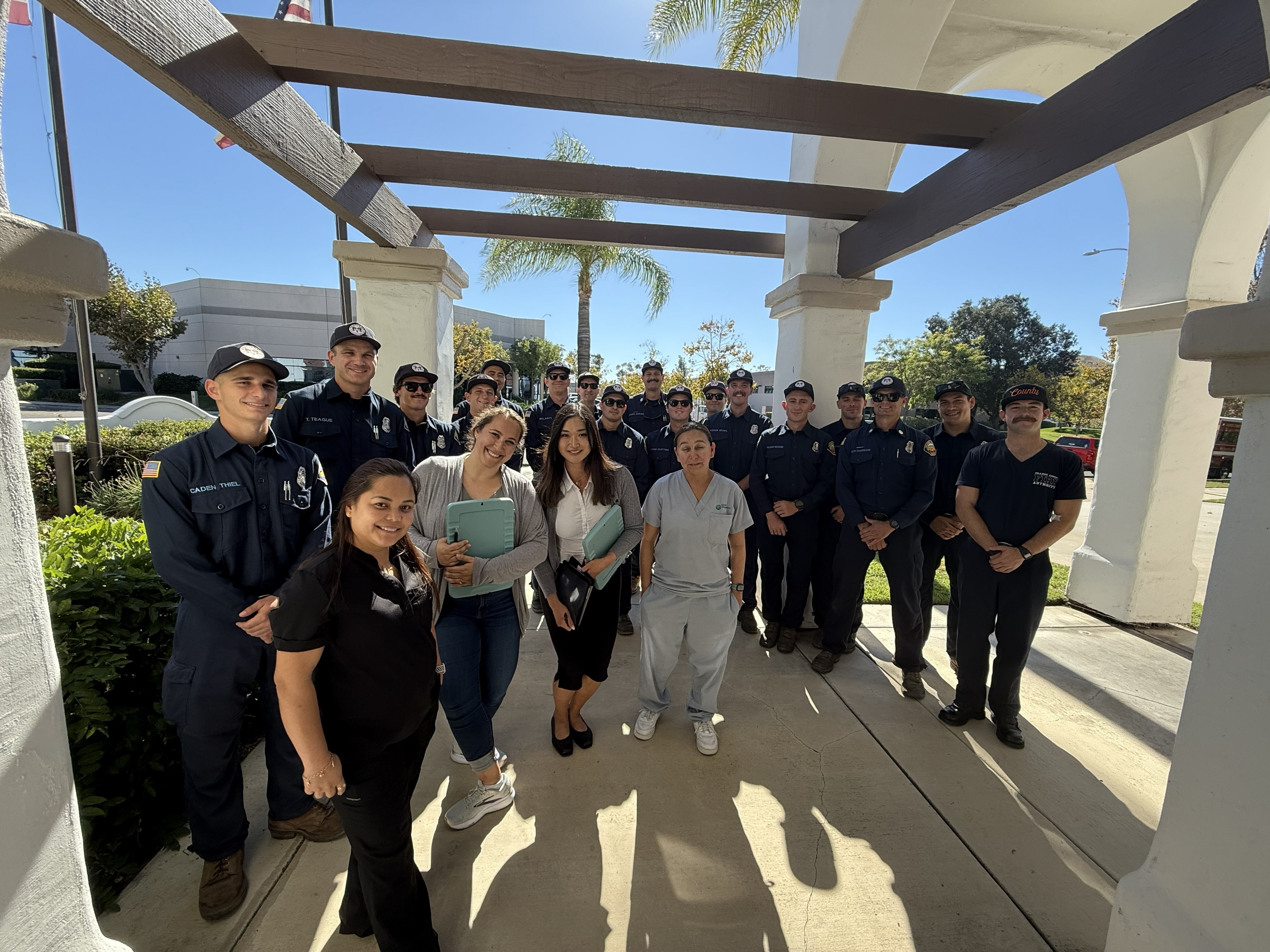 A group of researchers, including fire service members, posing for a photograph outside under a structure with greenery and architectural columns.