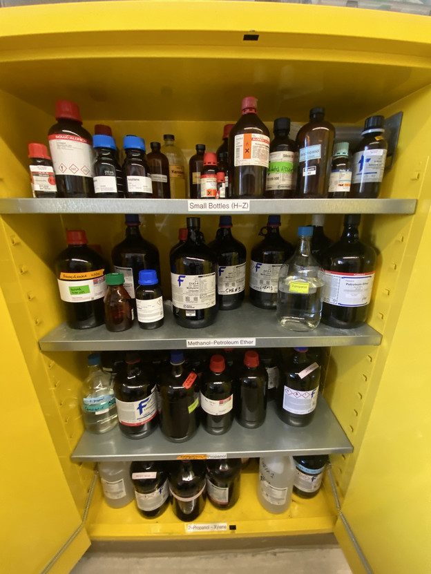 An image of a yellow cabinet with 4 shelves filled with chemical containers.