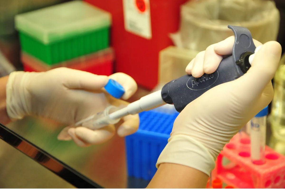 Close up image of a person with white gloves holding a device that is pour chemicals into a container.